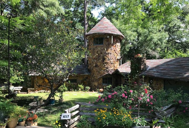 Tiny house with a unique tower design in a lush garden setting.