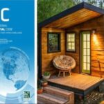 Small modern tiny house with wooden exterior and large windows, on a raised foundation.