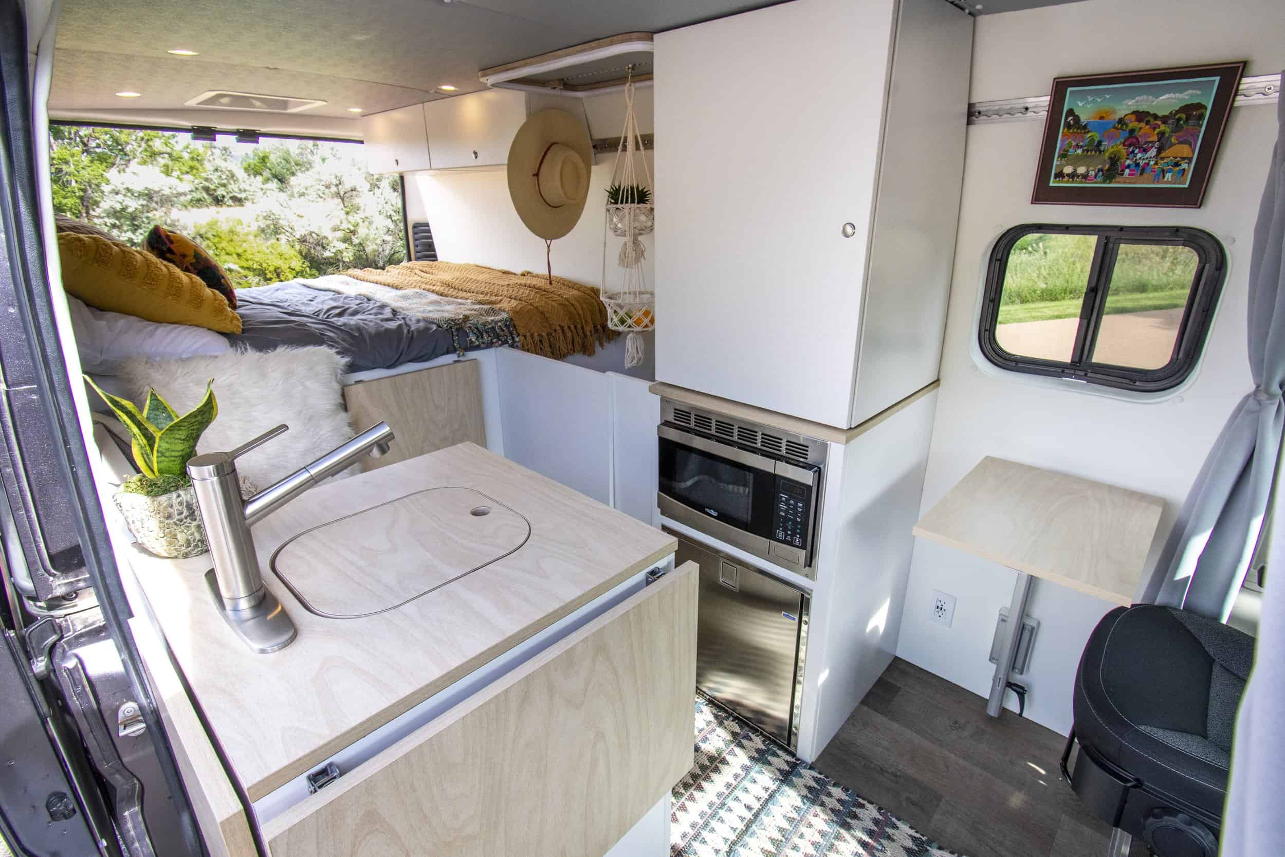 Efficient tiny house interior featuring a small kitchen, bed area, and workspace with natural light.