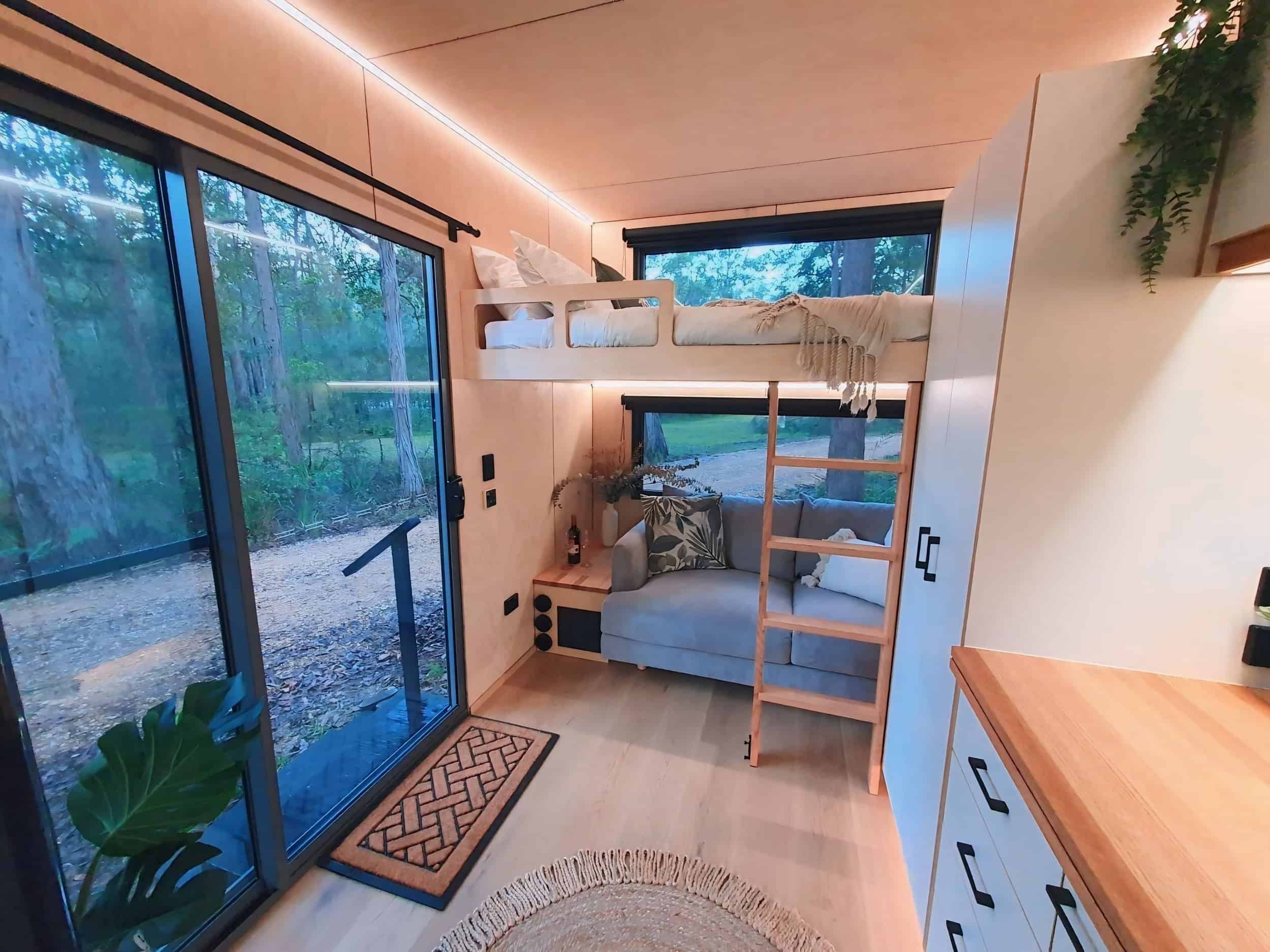 Cozy tiny house interior featuring a bunk bed and large windows with forest view.