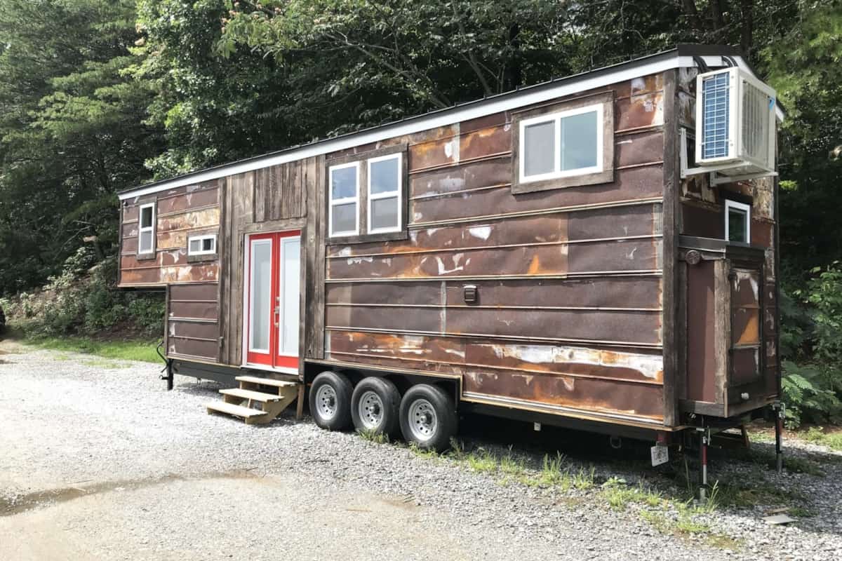 Rustic tiny house on wheels with weathered wood siding and modern windows.
