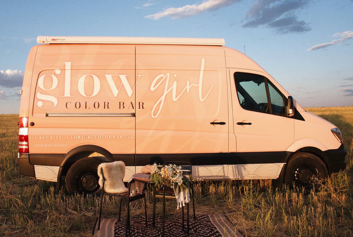 Pink van with "Glow Girl" logo parked in field with outdoor setup.