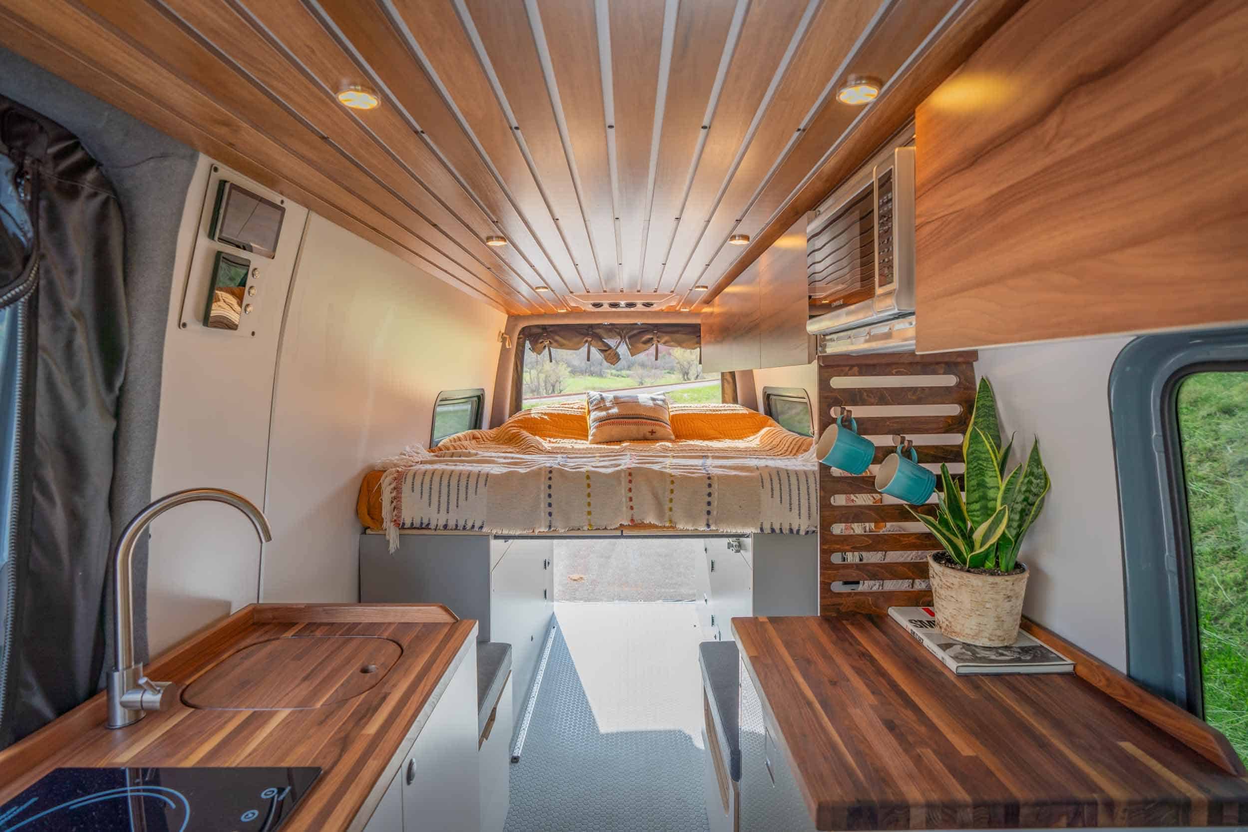 Tiny house interior featuring a cozy loft bed, wooden ceiling, and compact kitchen area.