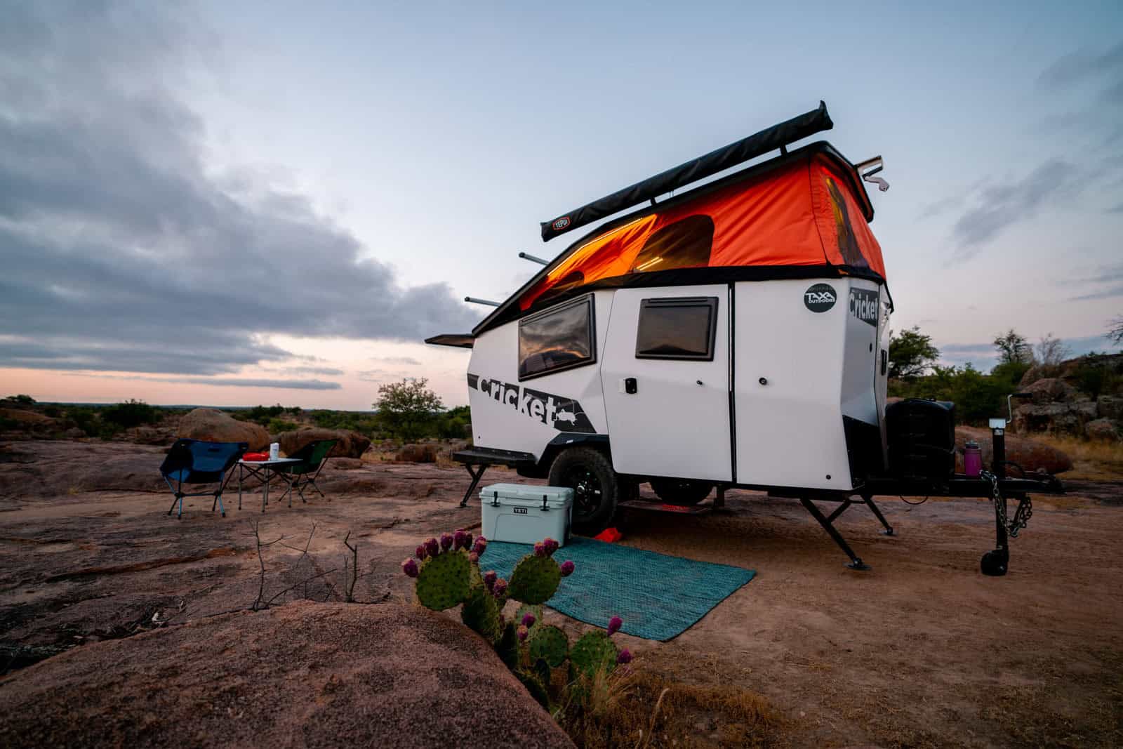 Compact tiny house with rooftop solar panel in a desert setting at sunset.