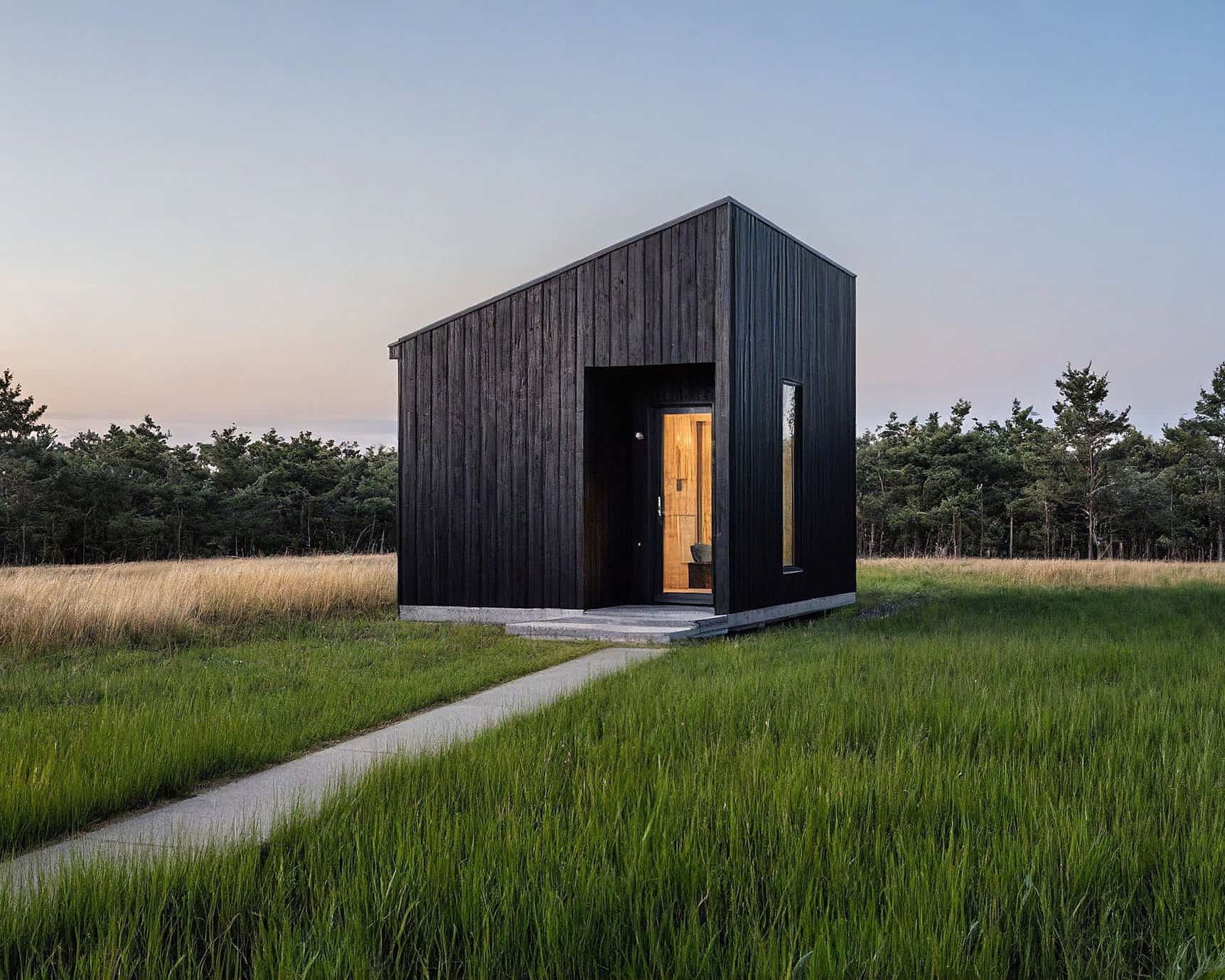 Tiny house with black exterior in a grassy field at sunset.