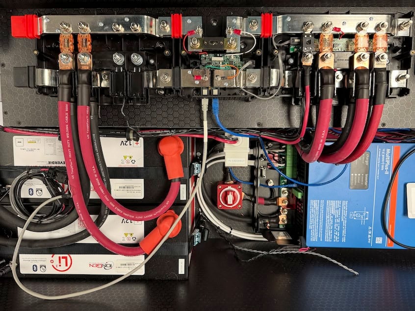 Electrical system inside a tiny house showing batteries, wiring, and circuit breakers.