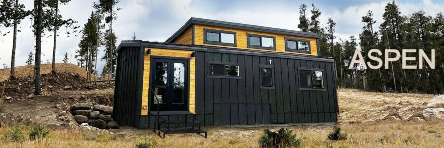 Black tiny house with yellow accents and large windows in a natural setting.