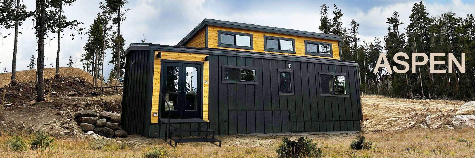 Black tiny house with yellow accents and large windows in a natural setting.