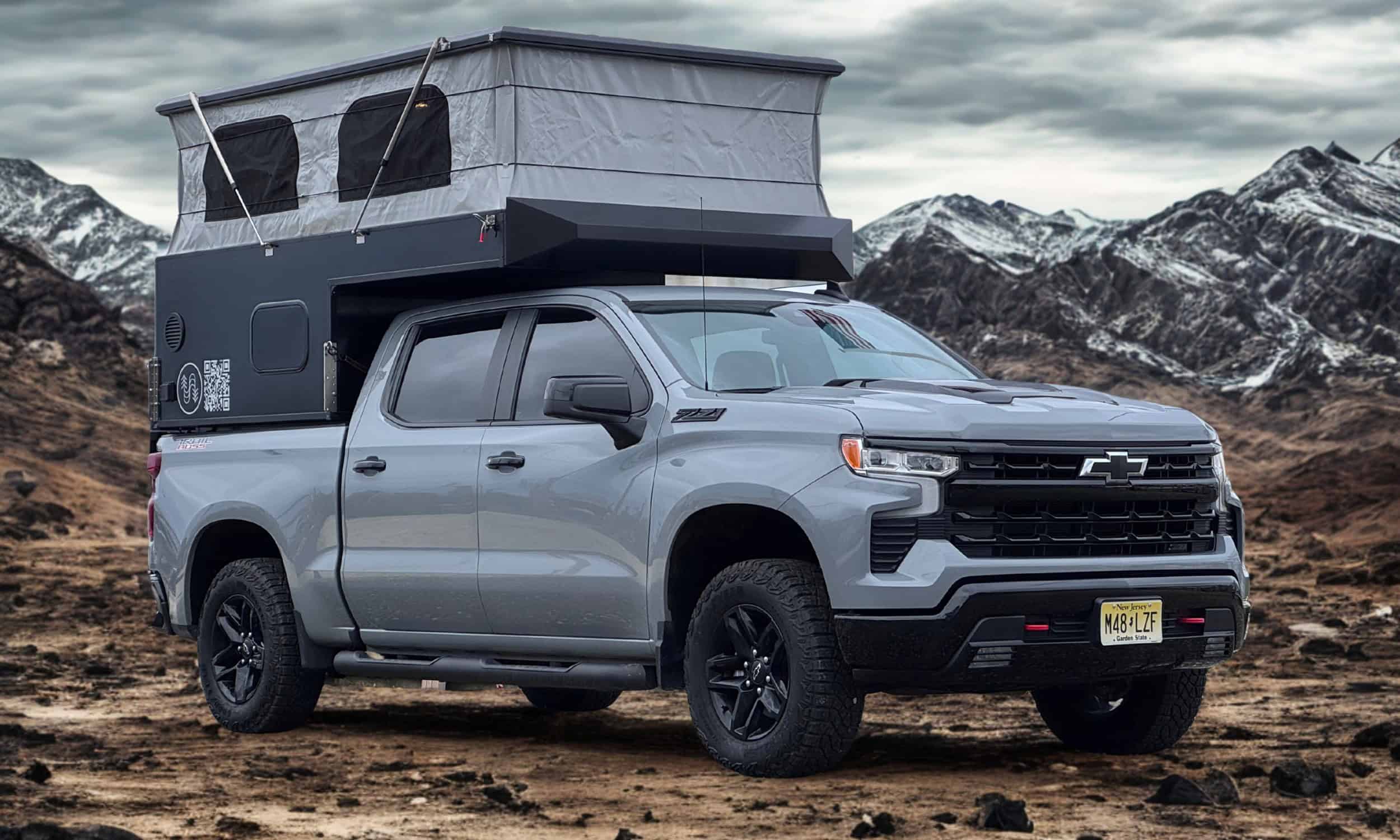 Black Big Ripper slide-in truck camper on a full-size pickup, pop-top raised, parked in the mountains