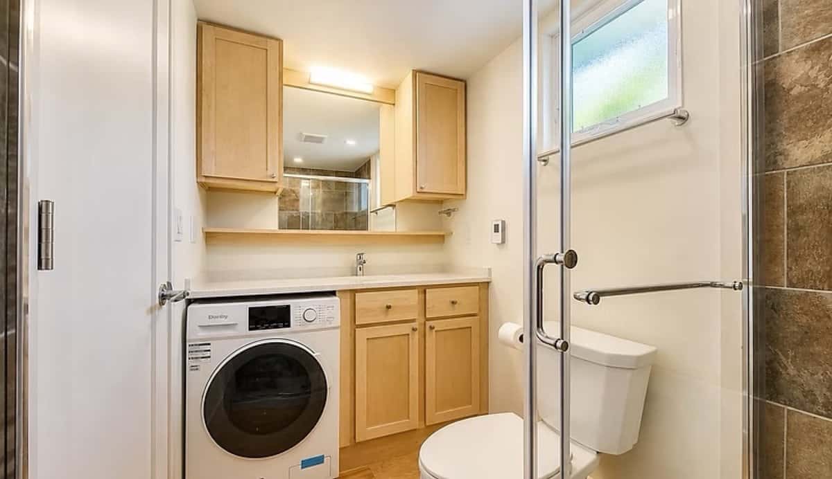 Ensuite bathroom with a maple vanity, built-in washer and dryer, glass walk-in shower, and toilet in the SHORELINE Glass House Lot 21