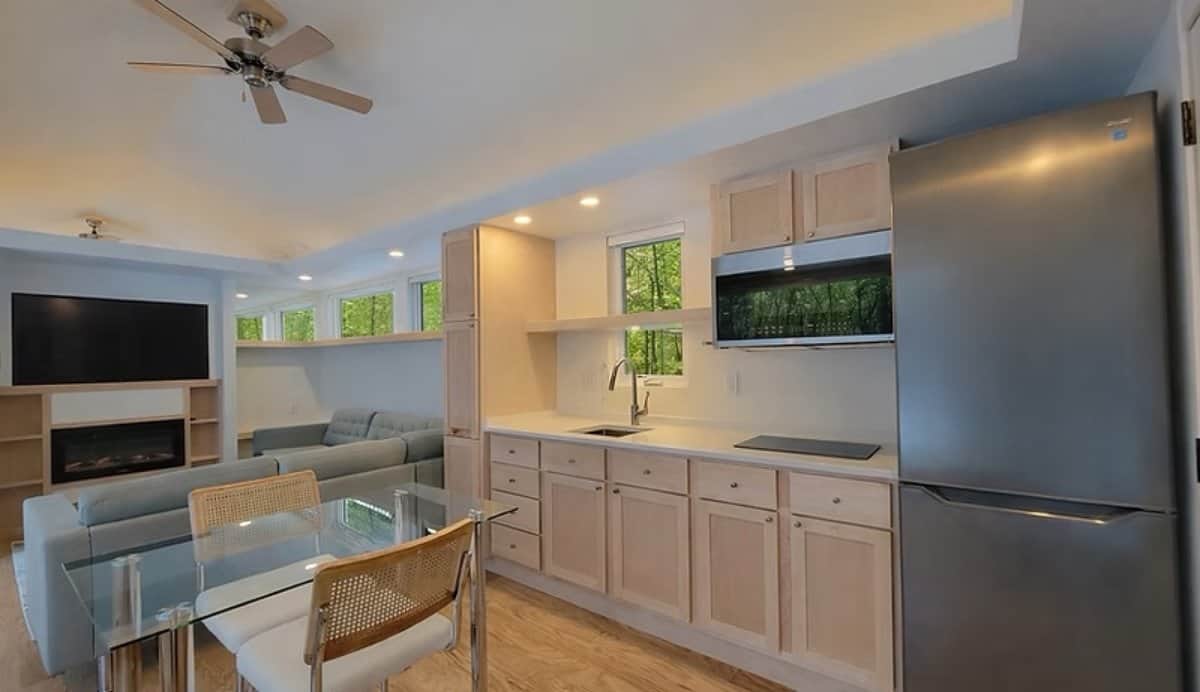 Open living area with a stainless steel kitchen, induction cooktop, glass dining table, sectional couch, and fireplace in the SHORELINE Glass House Lot 21