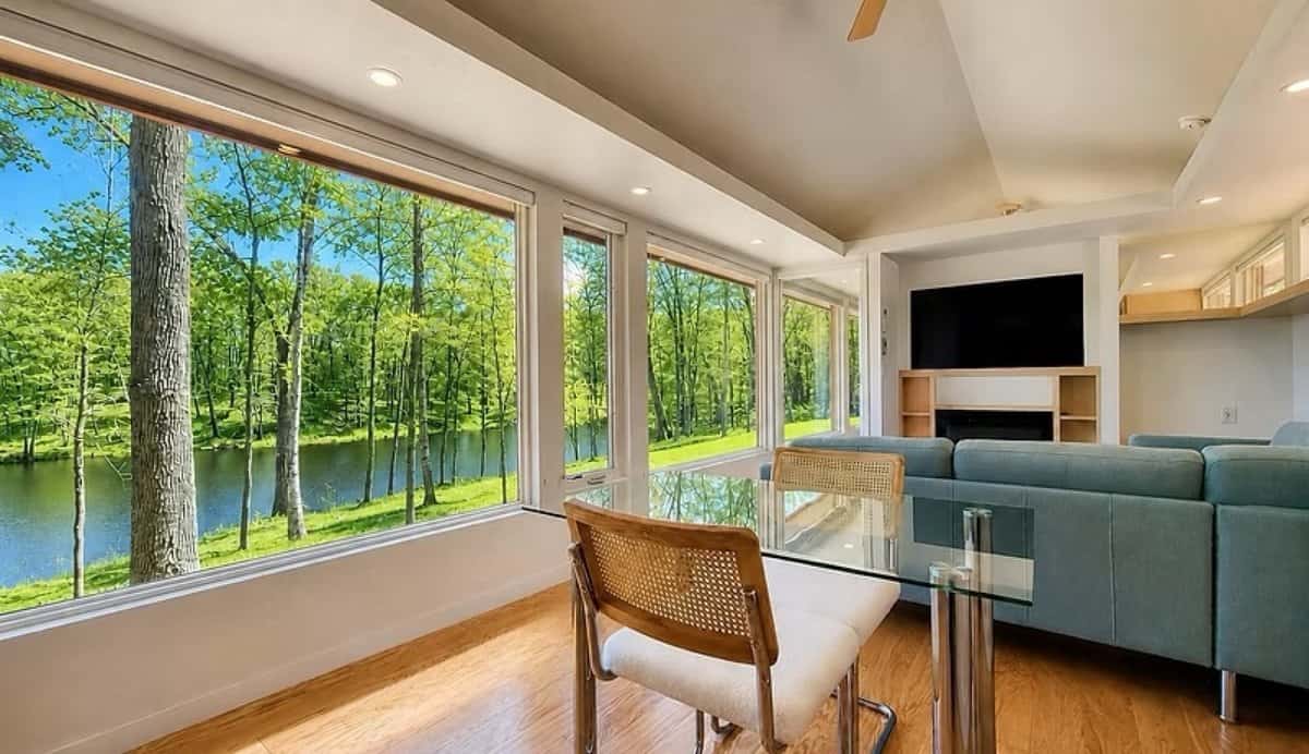 Living room with a 30-foot wall of glass framing Lost Lake, a sectional couch, fireplace, and Smart TV in the SHORELINE Glass House Lot 21