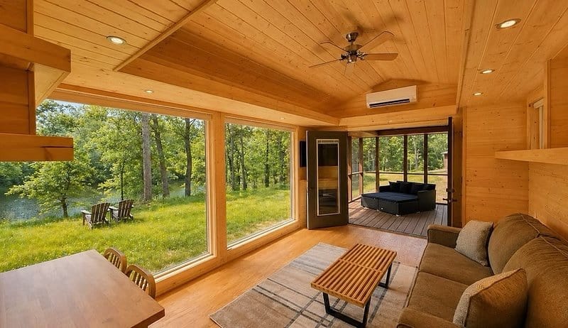 Living room with a corner wall of floor-to-ceiling glass overlooking the wooded lakeshore at the Shoreline Lot 16