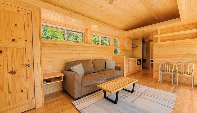 Open living area with a gray loveseat under clerestory windows and the kitchen and dining nook beyond at the Shoreline Lot 16