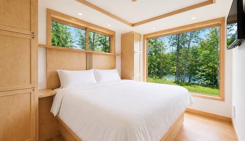 King bedroom with built-in maple cabinetry, Smart TV, and large picture windows facing the trees and lake at the Shoreline Lot 17