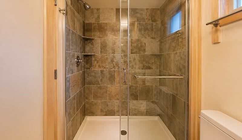 Walk-in tile shower with a glass sliding door and earth-toned stone tile at the Shoreline Lot 17