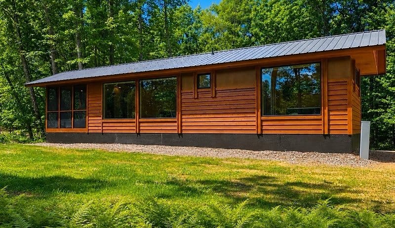 Shoreline cabin exterior with wood siding, metal roof, and a window wall among the trees at Canoe Bay Village Lot 23