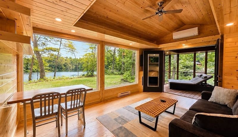 Light-filled great room with a window wall facing Lost Lake, sofa, dining nook, and screened porch beyond at the Shoreline Lot 23