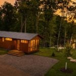 Shoreline cabin exterior with wood siding, metal roof, and screened porch at sunset on Lost Lake, Canoe Bay Village Lot 24