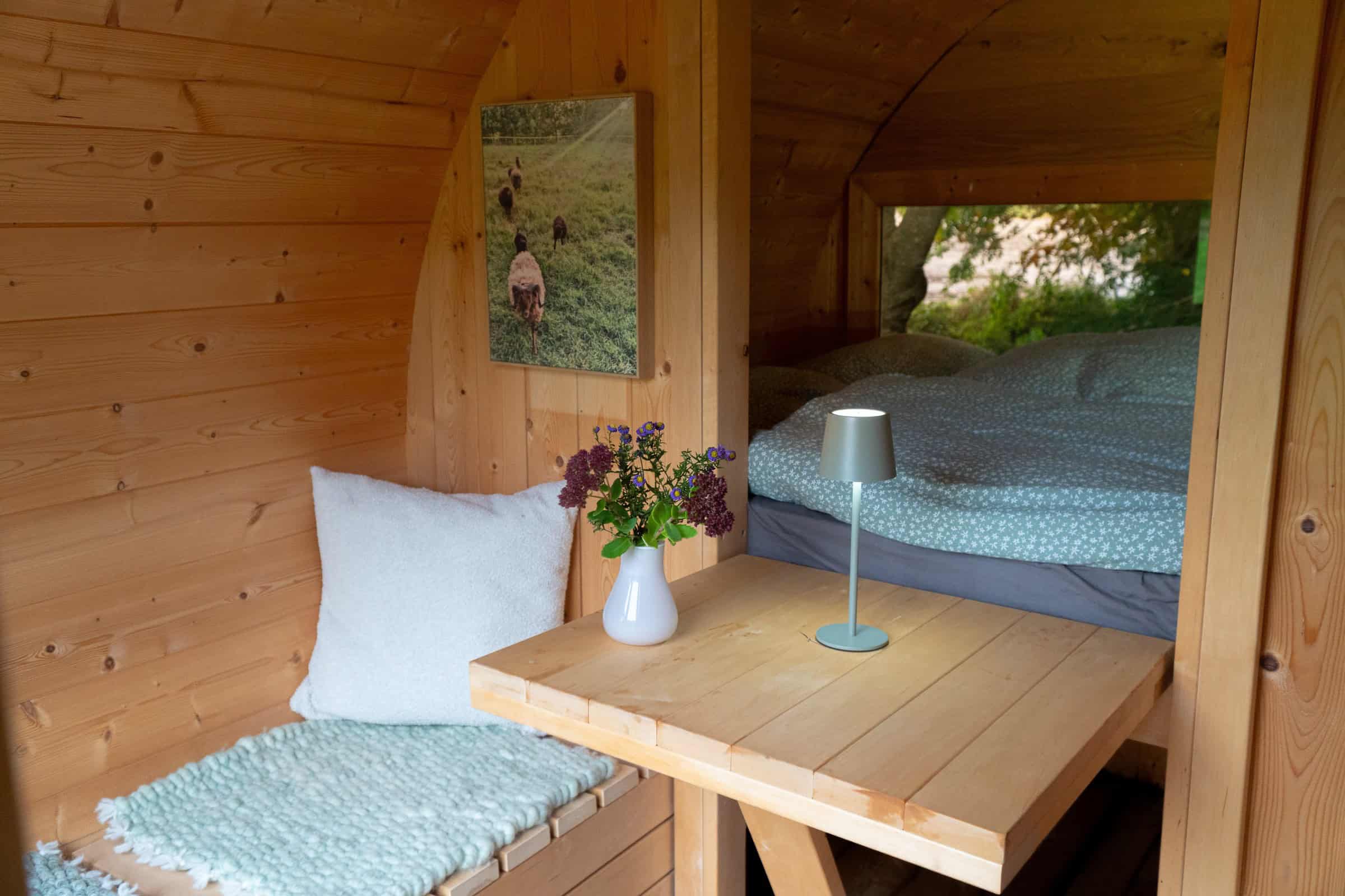 Curved wood cabin interior: bench and table, loft bed nook, sheep art on the partition