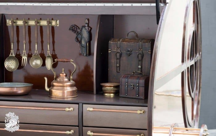 Close-up of brass utensils, a copper kettle, and vintage chests in the steampunk teardrop trailer galley