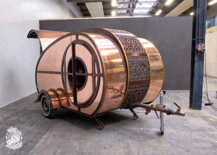 Shiny copper exterior of the steampunk teardrop trailer with a round porthole window and decorative filigree band