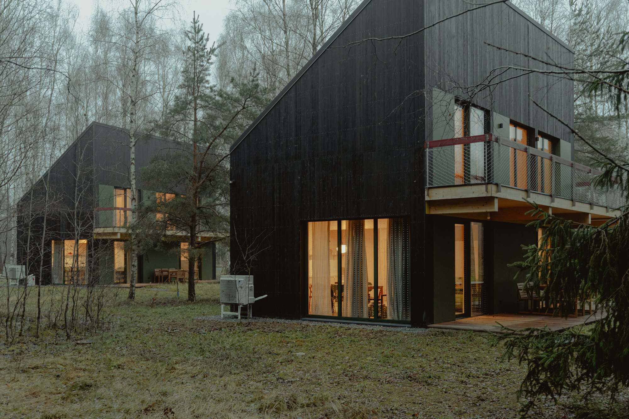 Two black Studzienno 27 cabins among birch at dusk, warm interior light in the glass and a balcony on each
