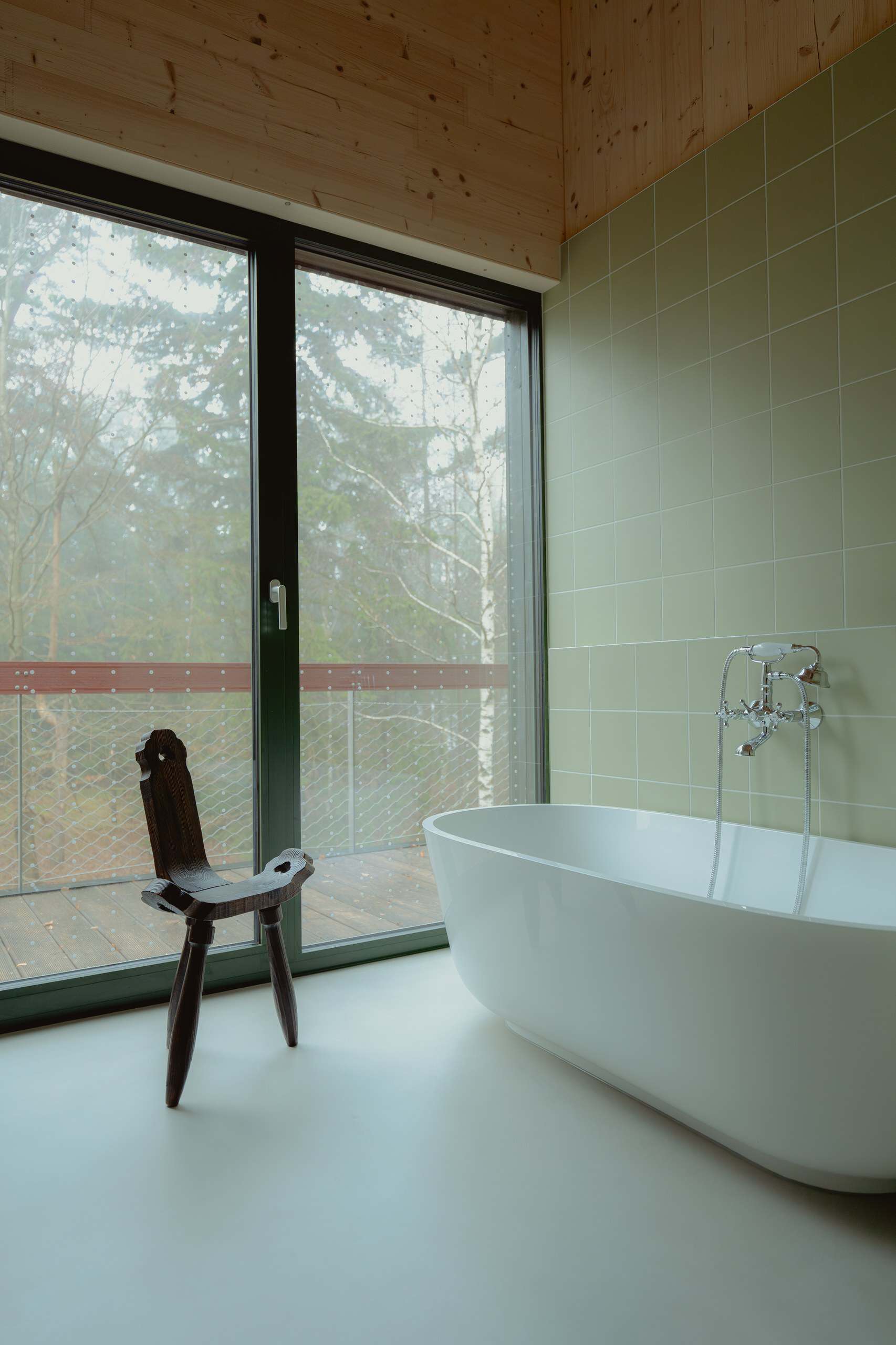 Freestanding bathtub in a Studzienno 27 cabin aimed at forest glass and a deck