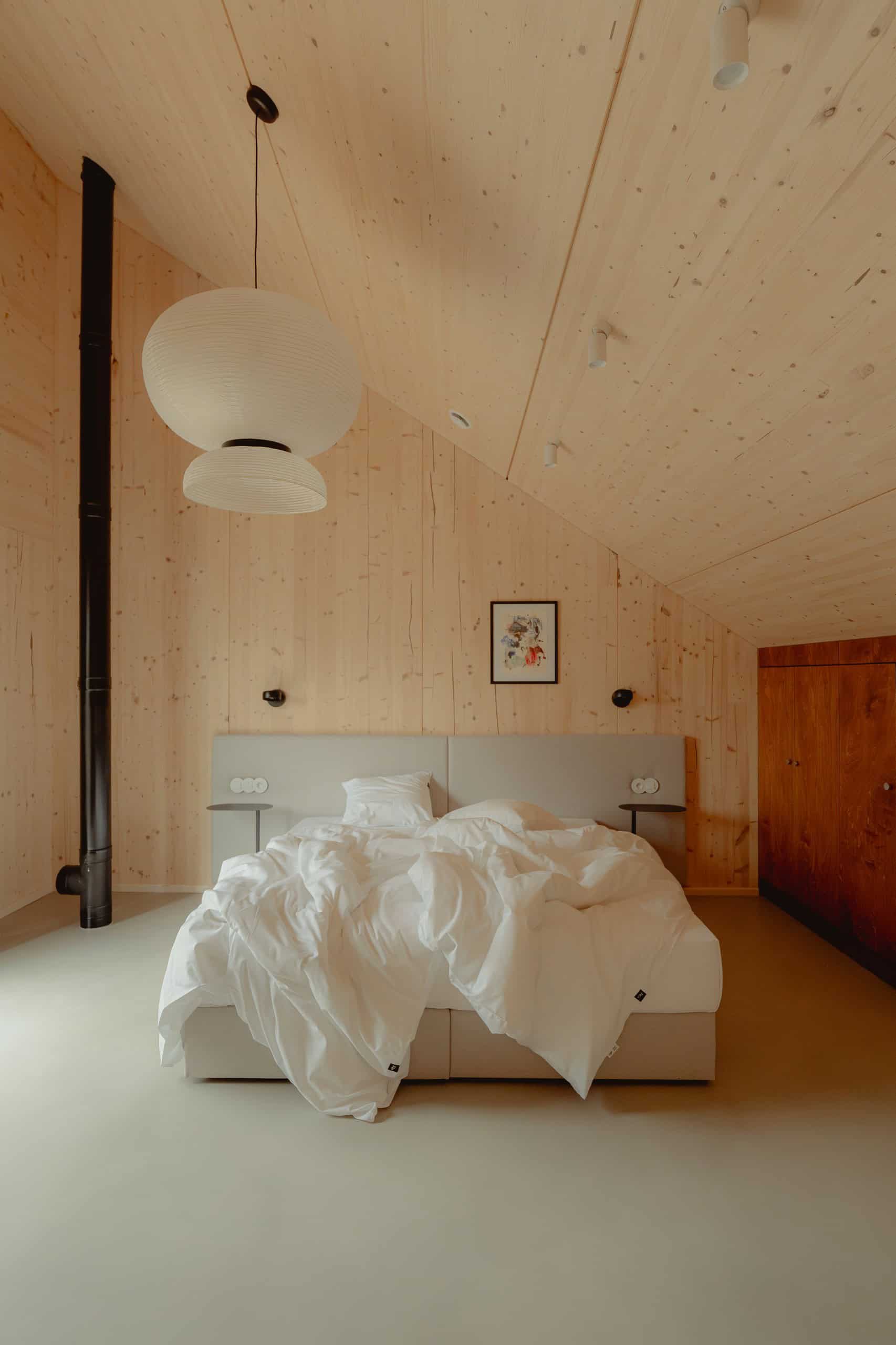 Bedroom in a Studzienno 27 cabin with a bed under a sloped CLT ceiling