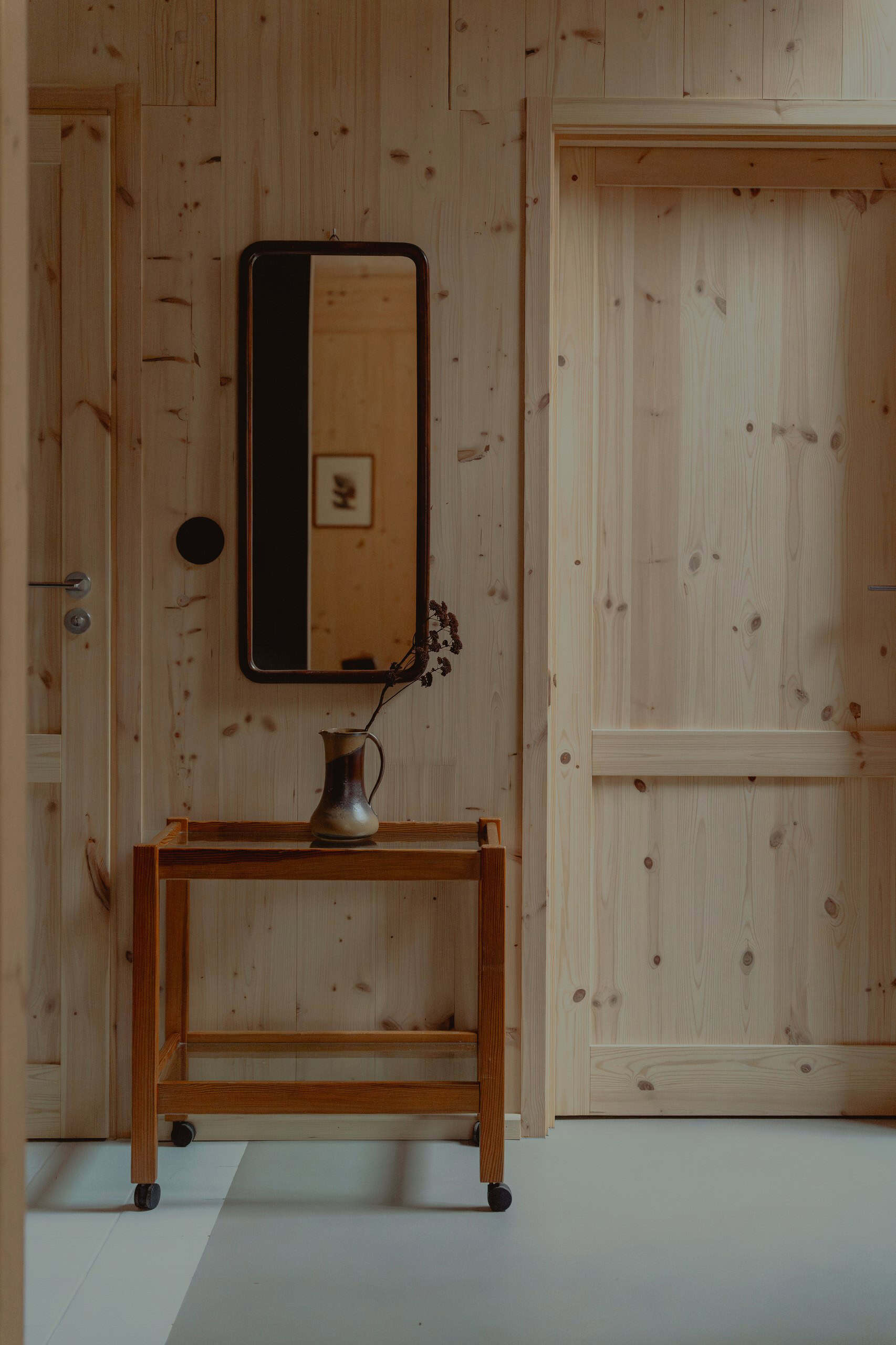 Exposed CLT walls and wood doors in a Studzienno 27 cabin, with a small cart and a mirror