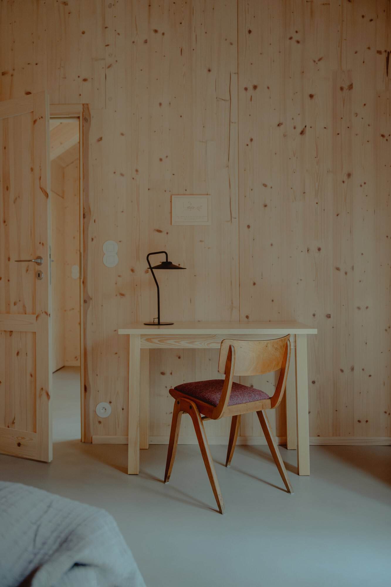 Wood desk and upholstered chair against a CLT wall in a Studzienno 27 bedroom, with the corner of a bed in the foreground