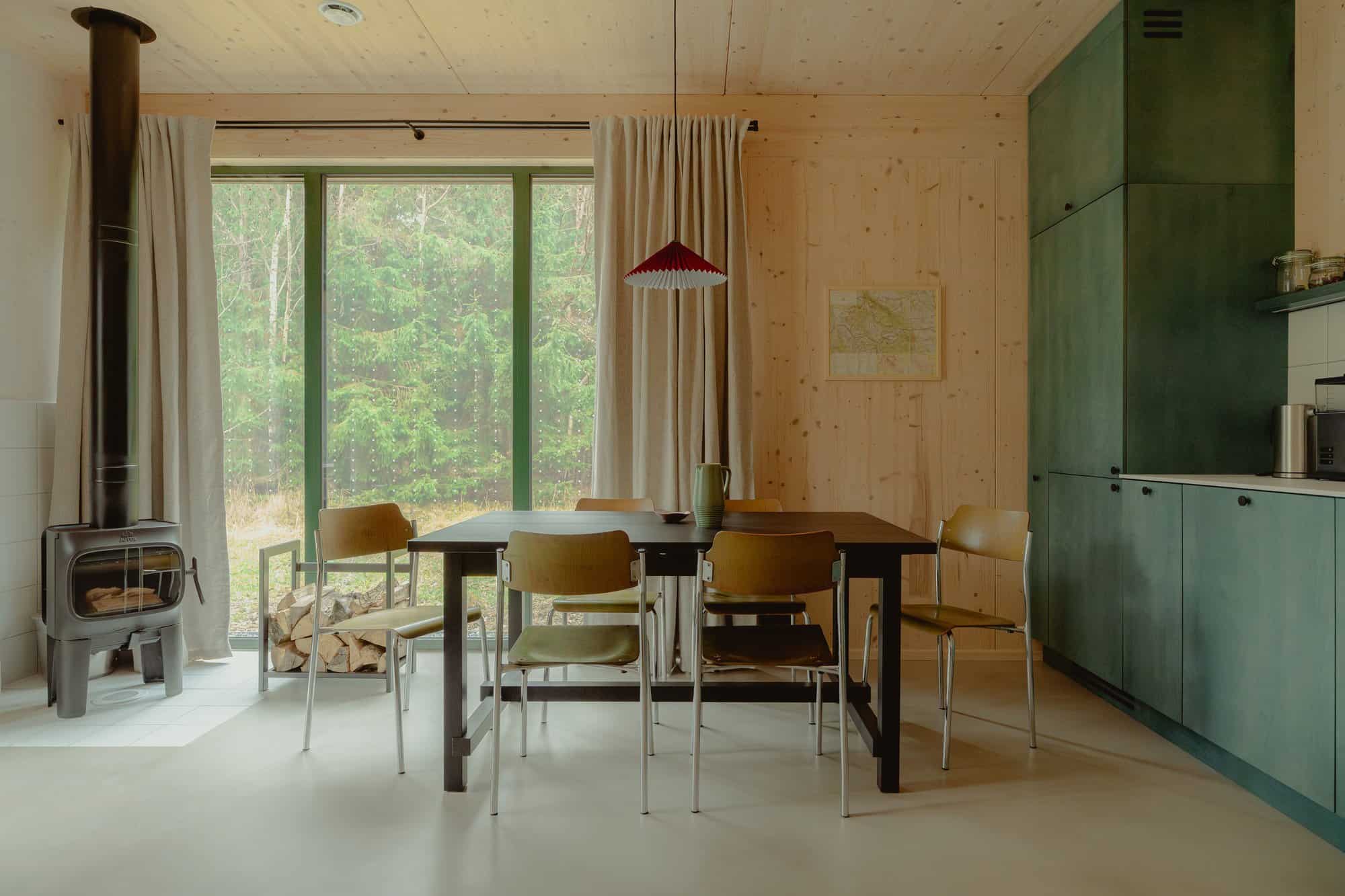 Dining table and forest-green kitchen cabinets with a black stove and forest glass in a Studzienno 27 cabin