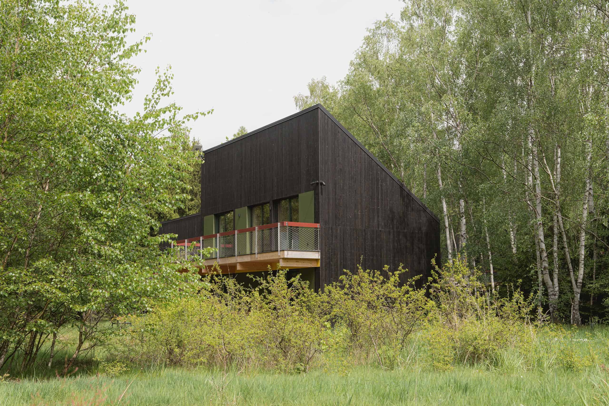 One two-level black Studzienno 27 cabin with a balcony, mesh rail, and forest behind