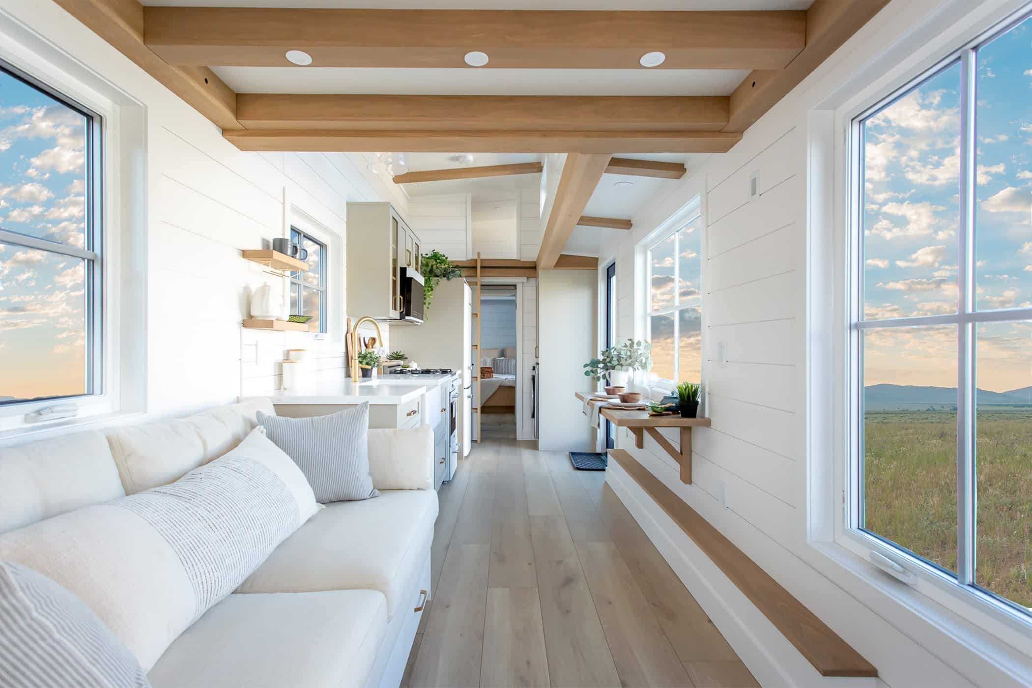 Summit Boho kitchen and living: white shiplap, wood ceiling beams, white sofa, farmhouse sink, gold faucet, green upper cabinets, view toward main-floor bedroom