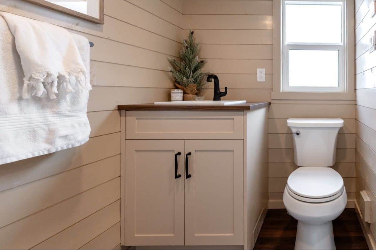 2026 Ruby bathroom: cream vanity, dark wood-look top, white rectangular sink, black faucet, toilet under a window