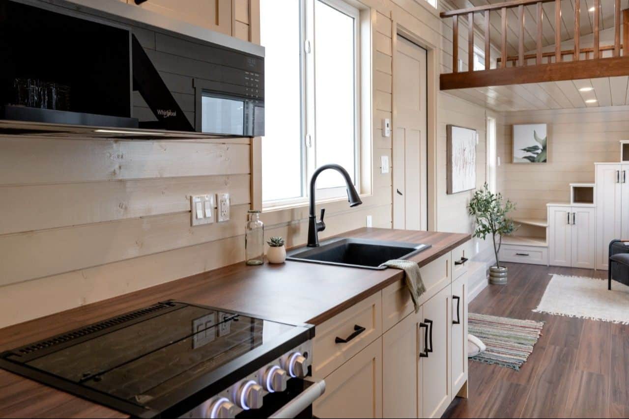 2026 Ruby kitchen: dark wood-look counter, black sink and faucet, cream shaker cabinets, black microwave, range, window over the sink