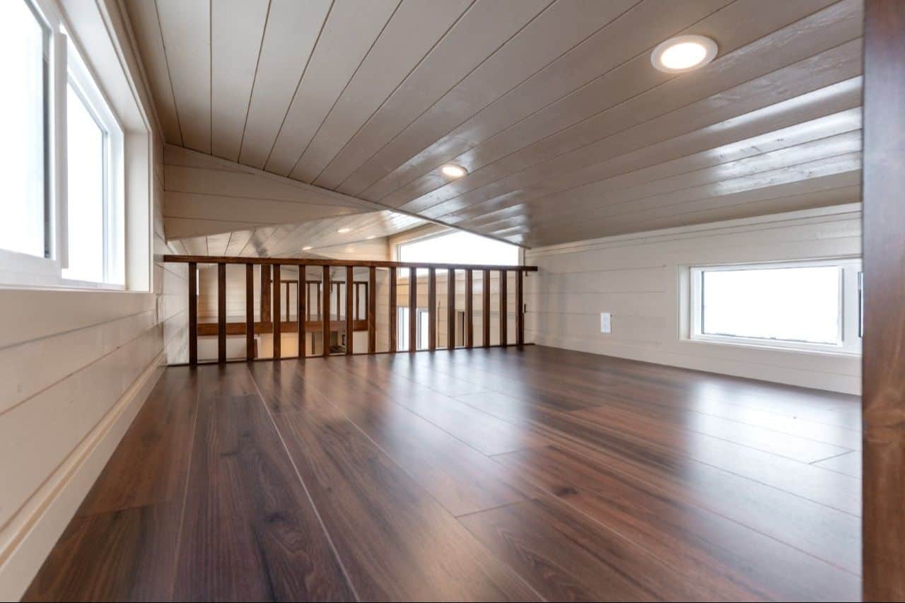 Inside a 2026 Ruby loft: dark plank floor, light shiplap pitch, dark vertical-slat rail, second loft rail visible across the well
