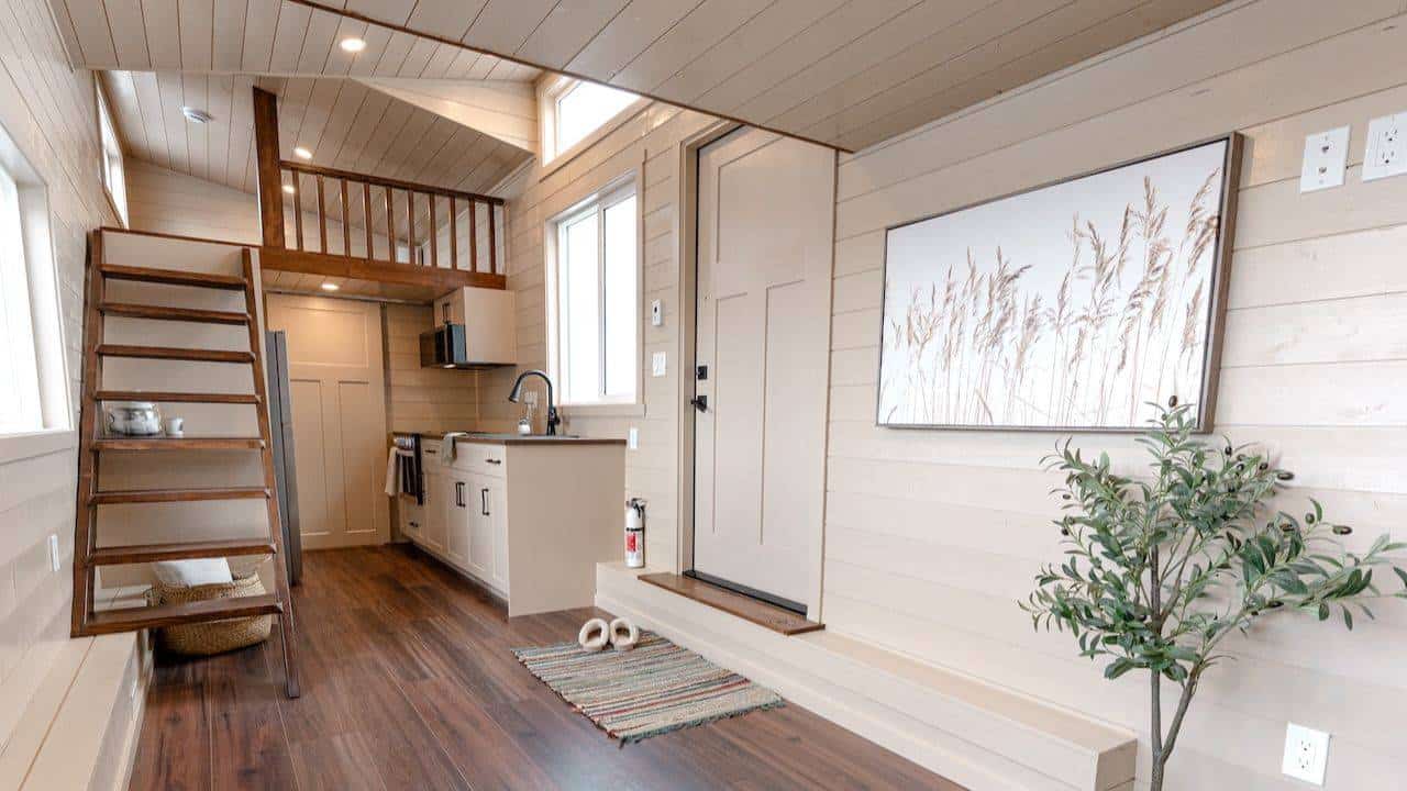 2026 Ruby interior: light shiplap, dark open-riser stair on the left, loft rail over a cream kitchen, craftsman door on the right