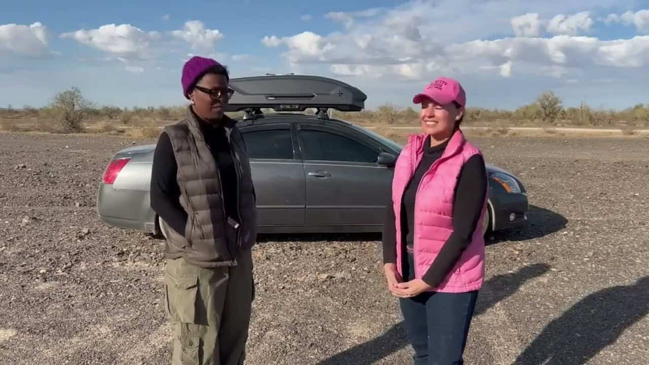 Tee and CheapRVliving host standing in front of the silver Maxima with roof box closed on desert floor