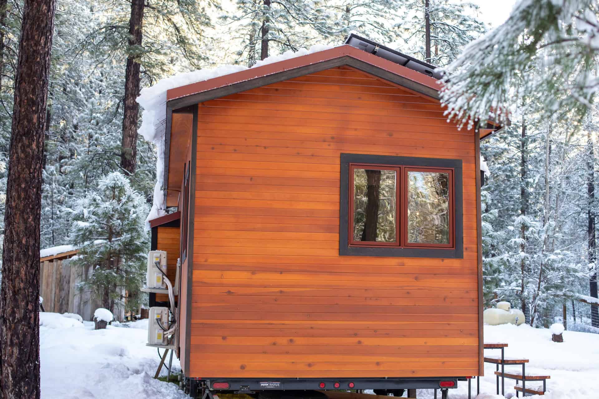 Tiny house with wooden exterior in a snowy forest setting.