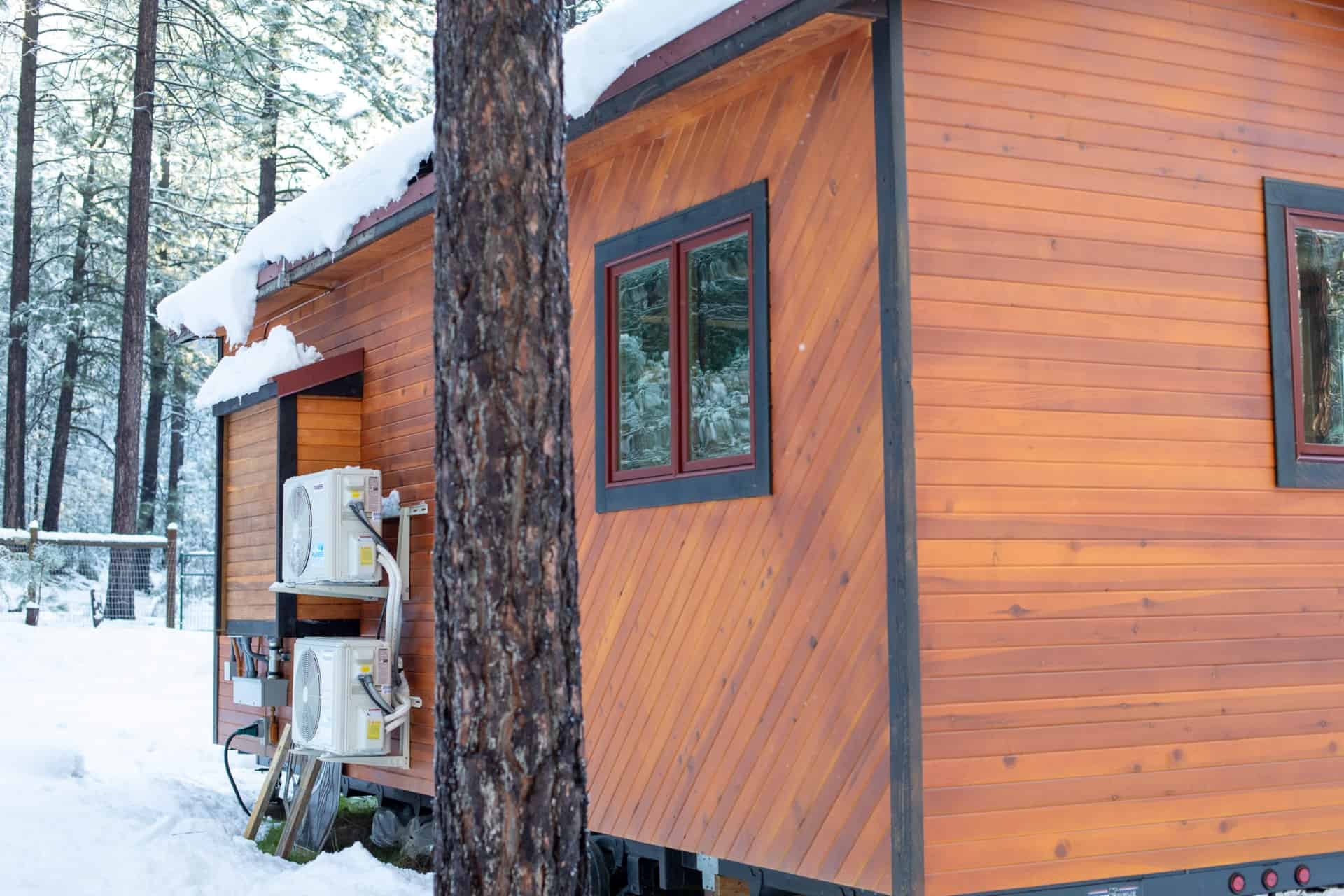 Tiny house with wooden exterior in snowy forest setting.
