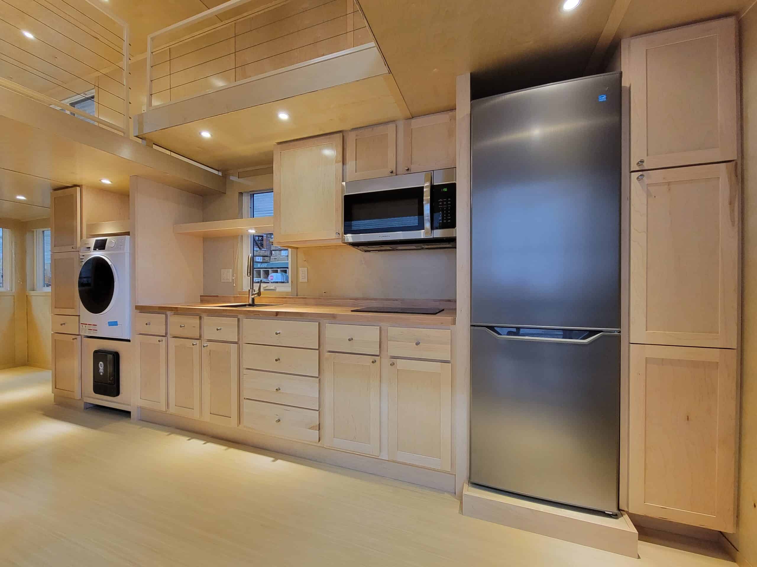 Compact tiny house kitchen with stainless steel fridge, microwave, and washer-dryer combo.