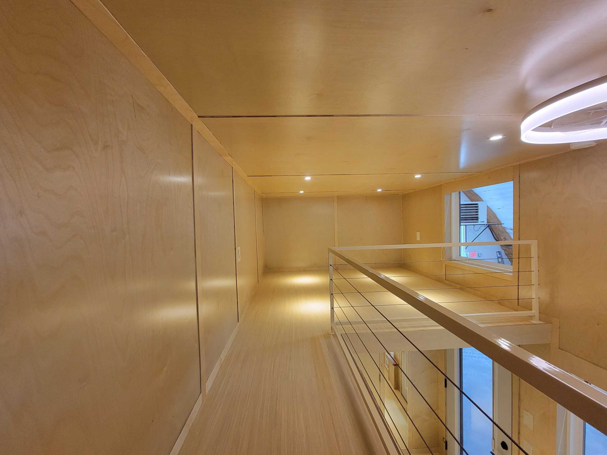 Bright tiny house interior with wooden walls and ceiling, featuring a staircase and large window for.