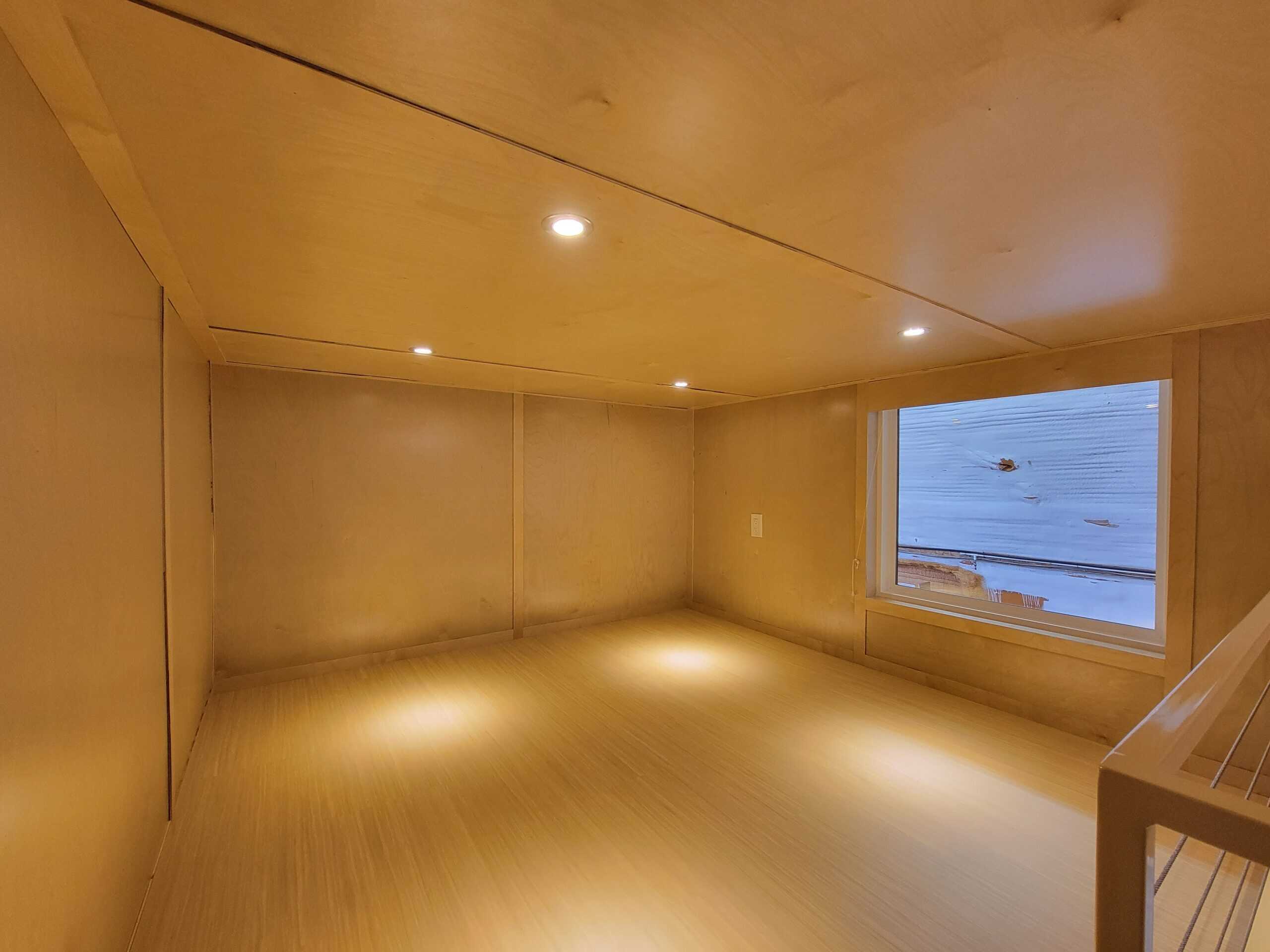 Interior of a tiny house showcasing wooden walls, ceiling, and flooring with a large window overlook.