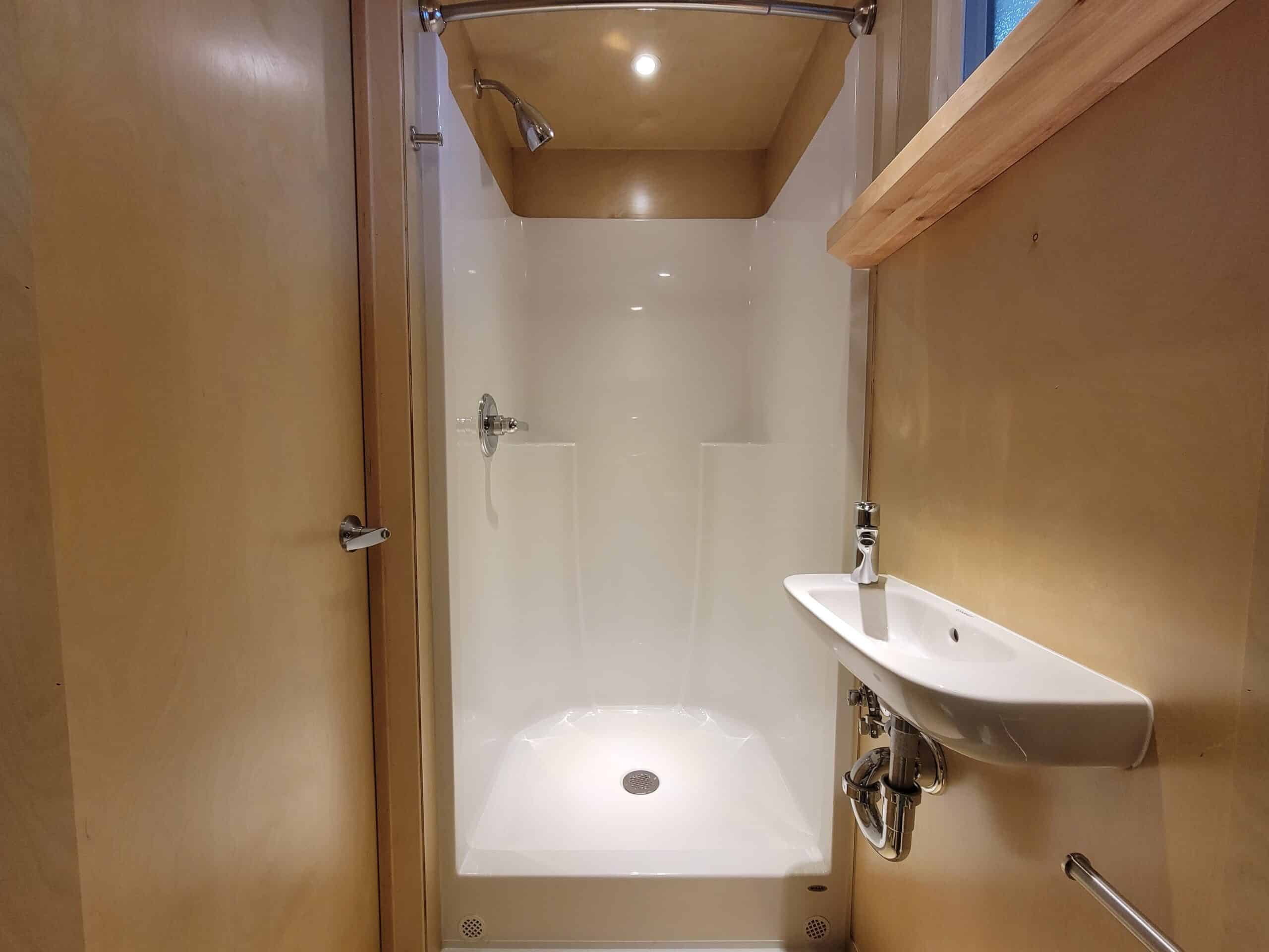 Compact tiny house bathroom with shower and small sink.
