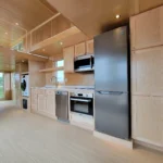 Modern tiny house kitchen with sleek appliances and light wood cabinetry.