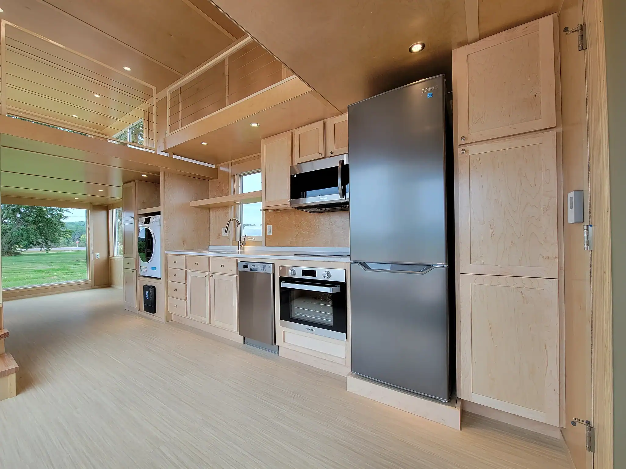Modern tiny house kitchen with sleek appliances and light wood cabinetry.