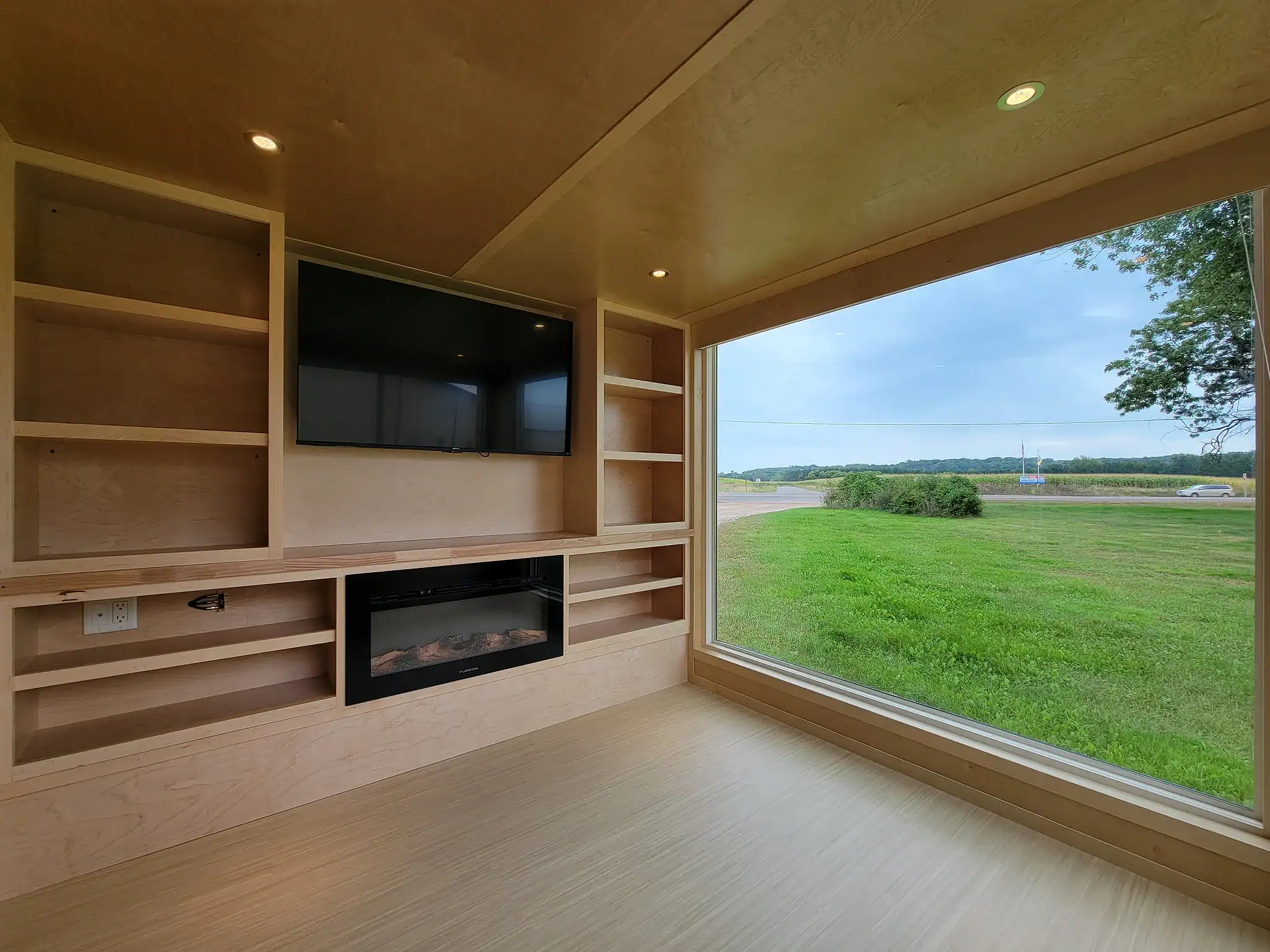 Interior of a tiny house with a large window overlooking green fields and a built-in entertainment c.