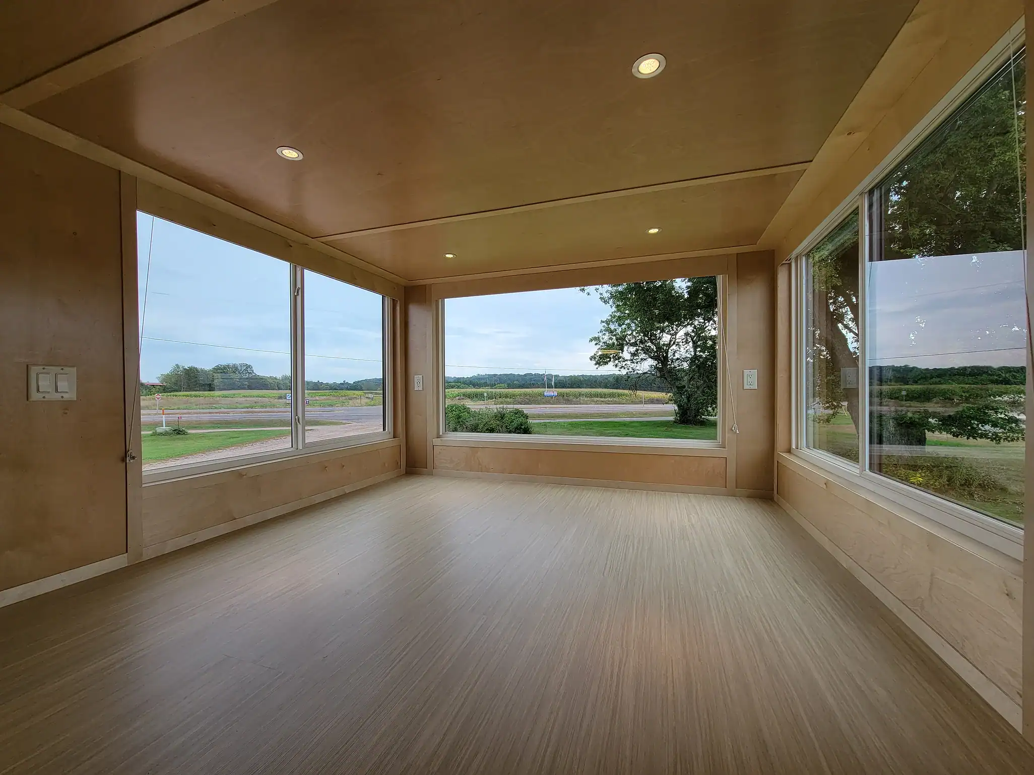 Bright interior of a tiny house with expansive windows showcasing outdoor landscape.