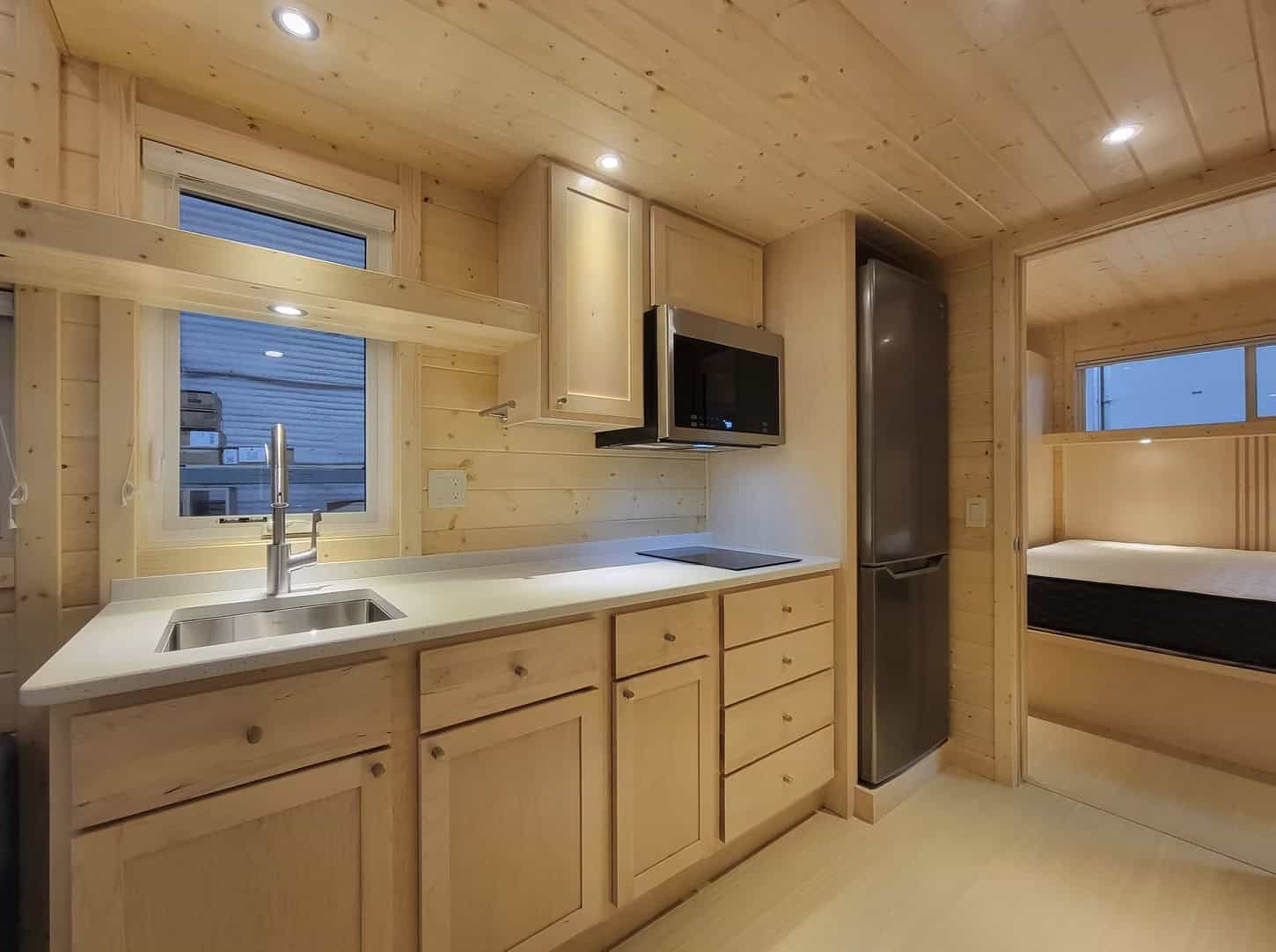 Compact tiny house kitchen with modern appliances and cozy sleeping nook.